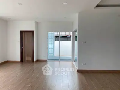 Spacious empty room with wooden flooring and sliding glass doors leading to a small balcony.