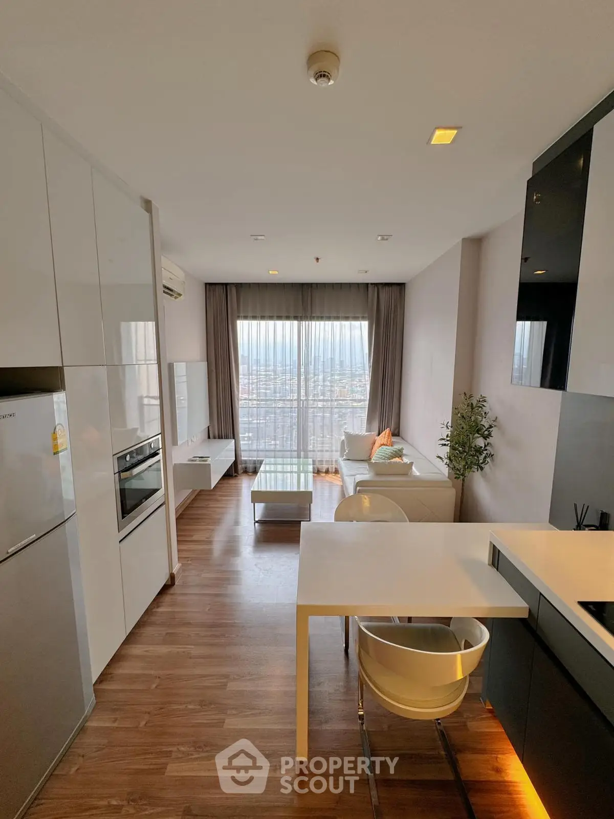 Modern living room with open kitchen and city view, featuring sleek furniture and natural light.