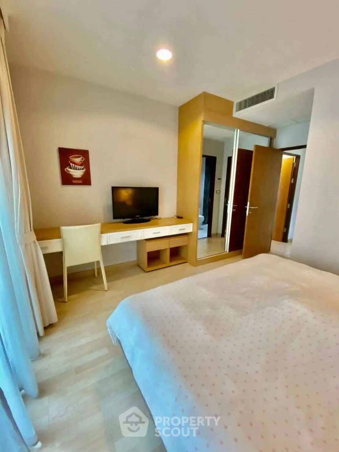 Cozy bedroom with modern decor, featuring a study desk and large mirror wardrobe, perfect for urban living.