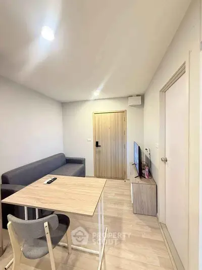 Modern living room with minimalist furniture and wooden flooring, featuring a cozy sofa and sleek TV setup.