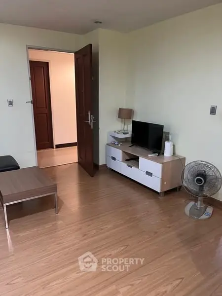 Cozy living room with wooden flooring, TV unit, and open door to hallway.