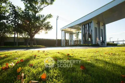 Modern building entrance with lush green lawn and trees, showcasing elegant architecture and serene surroundings.