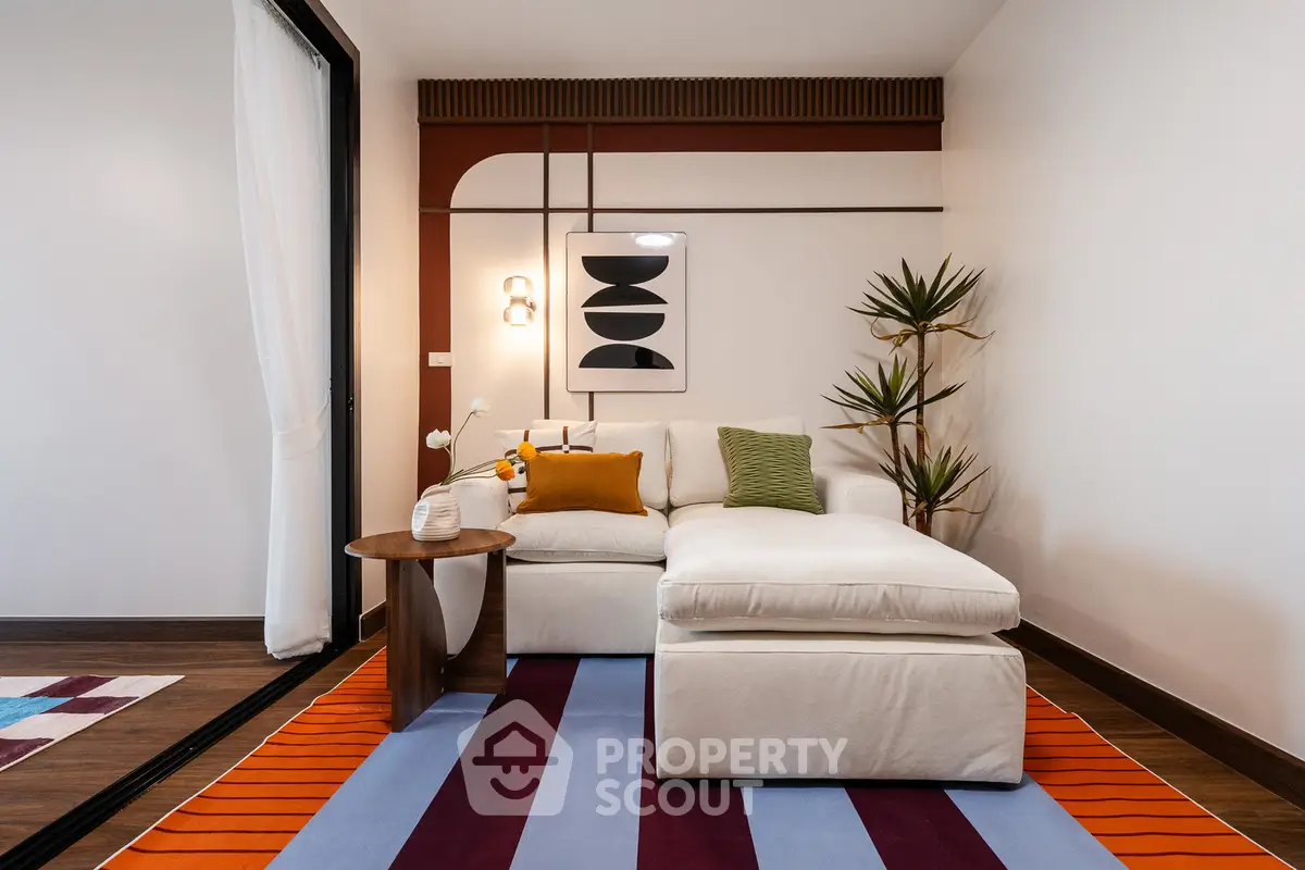 Stylish living room with modern decor and colorful rug, featuring a cozy white sofa and elegant wall art.