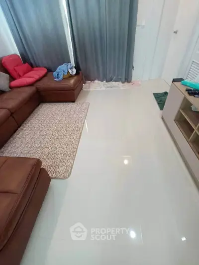 Spacious living room with modern brown leather sofa and sleek tiled flooring.