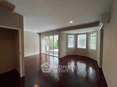 Spacious living room with hardwood floors and large windows offering natural light and garden view.