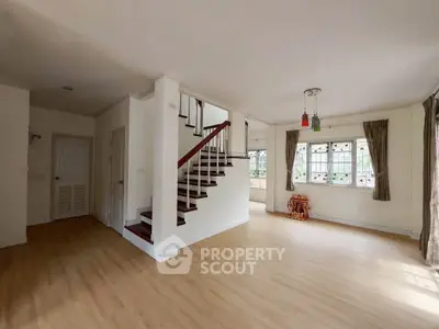Spacious open-plan living area with wooden staircase and large windows.