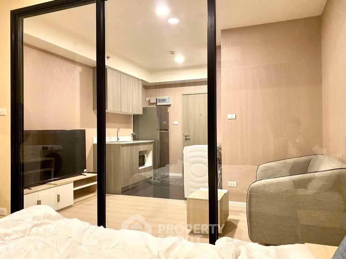 Modern studio apartment with glass partition, cozy living area, and compact kitchen.