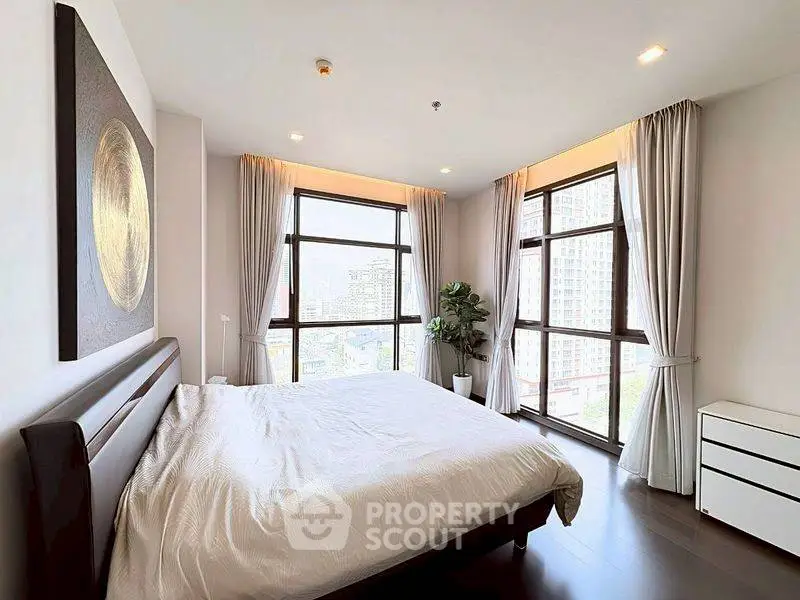 Spacious bedroom with large windows offering city views, modern decor, and natural light.