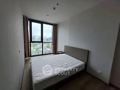 Spacious bedroom with large window offering stunning city views in modern apartment.