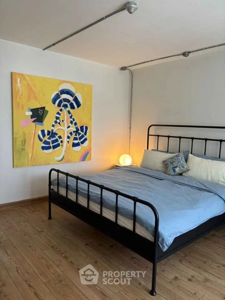 Modern bedroom with stylish artwork and cozy lighting, featuring a metal bed frame and wooden flooring.