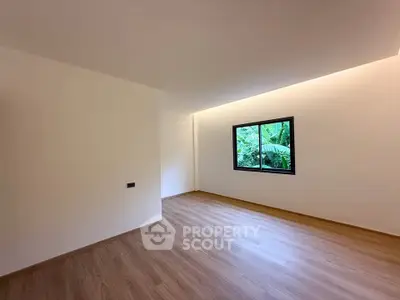 Spacious empty room with wooden flooring and large window overlooking greenery, perfect for customization.