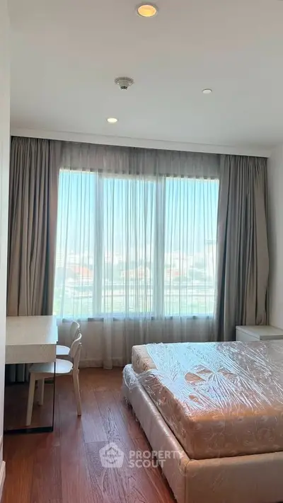 Bright bedroom with large window and wooden flooring, featuring a bed and study desk.