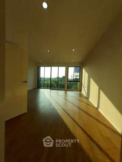 Spacious living room with large windows and wooden flooring, offering abundant natural light and scenic views.
