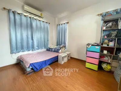 Cozy bedroom with wooden flooring and ample natural light, featuring a comfortable bed and organized storage.