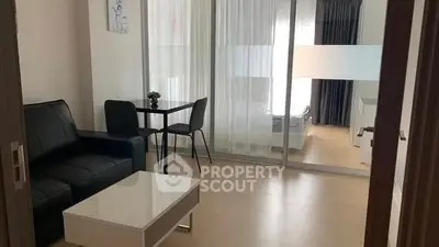 Modern living room with sleek furniture and glass partition leading to bedroom.