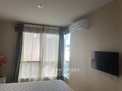 Cozy bedroom with natural light, featuring a wall-mounted TV and air conditioning unit.