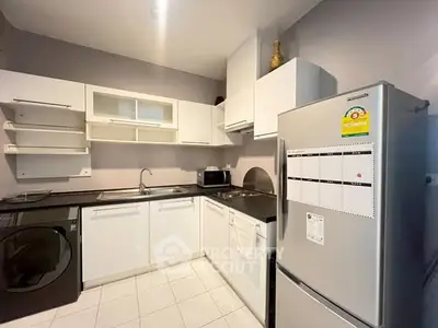 Modern kitchen with sleek white cabinets, stainless steel fridge, and washing machine in a compact layout.