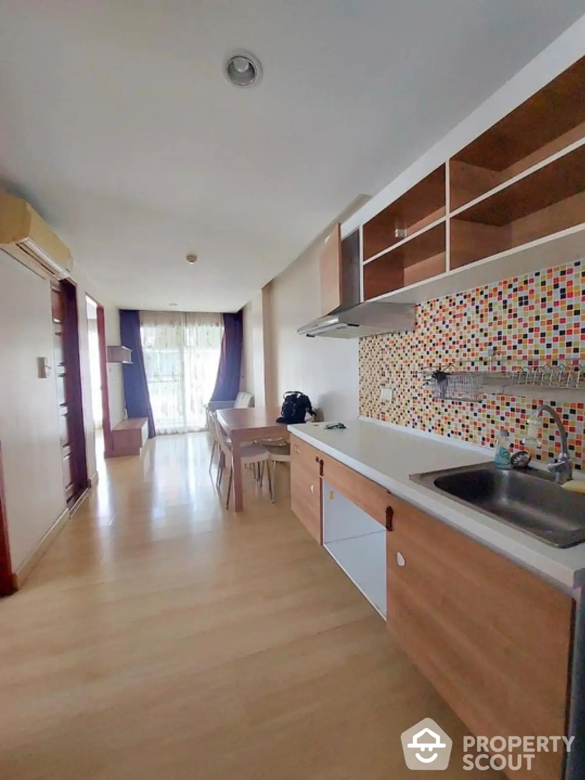 Modern open-layout kitchen with colorful backsplash and wooden cabinetry in a bright apartment.