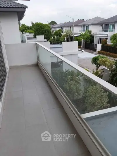 Spacious balcony with glass railing offering a serene view of suburban neighborhood.