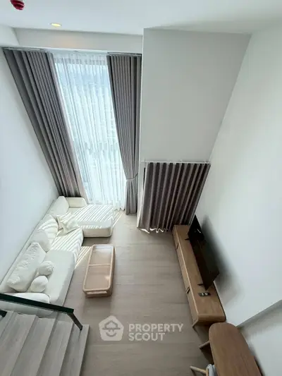 Modern living room with high ceiling and large window, featuring elegant curtains and cozy furniture.
