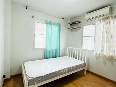 Bright bedroom with wooden flooring and air conditioning, featuring a single bed and colorful curtains.
