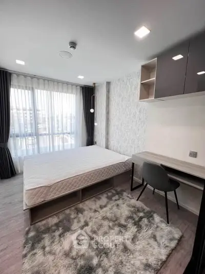 Modern bedroom with large window, stylish decor, and cozy rug in a contemporary apartment.