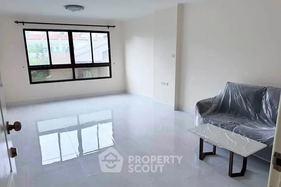 Spacious living room with large window and minimalistic furniture, offering ample natural light.