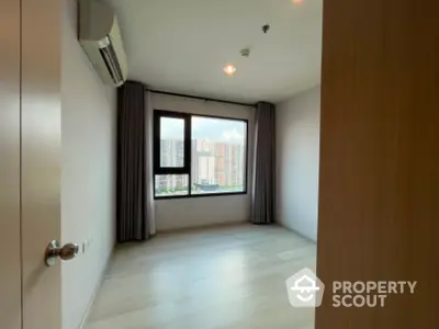 Spacious bedroom with large window offering city view in modern apartment.