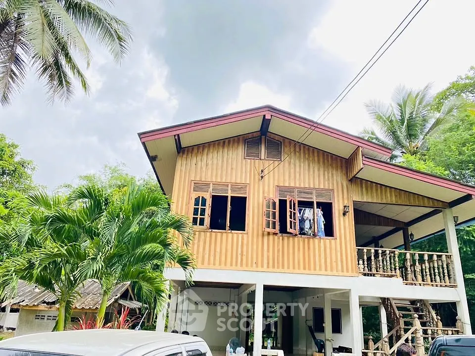 Charming two-story wooden house with lush greenery and tropical palm trees.