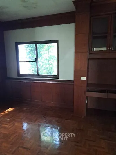 Spacious room with wooden flooring and large window, ideal for customization.