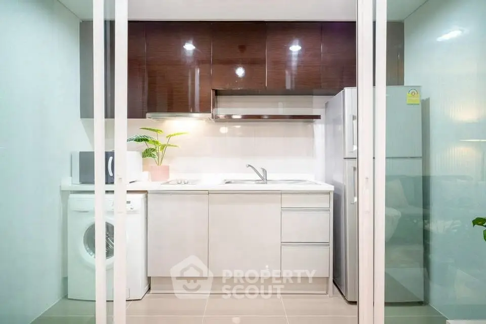 Modern kitchen with sleek cabinets, washing machine, and stainless steel fridge.