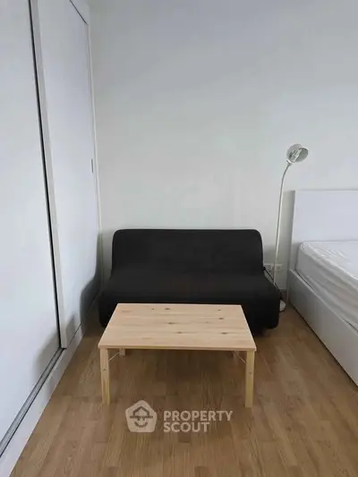 Minimalist bedroom with black sofa, wooden table, and white bed