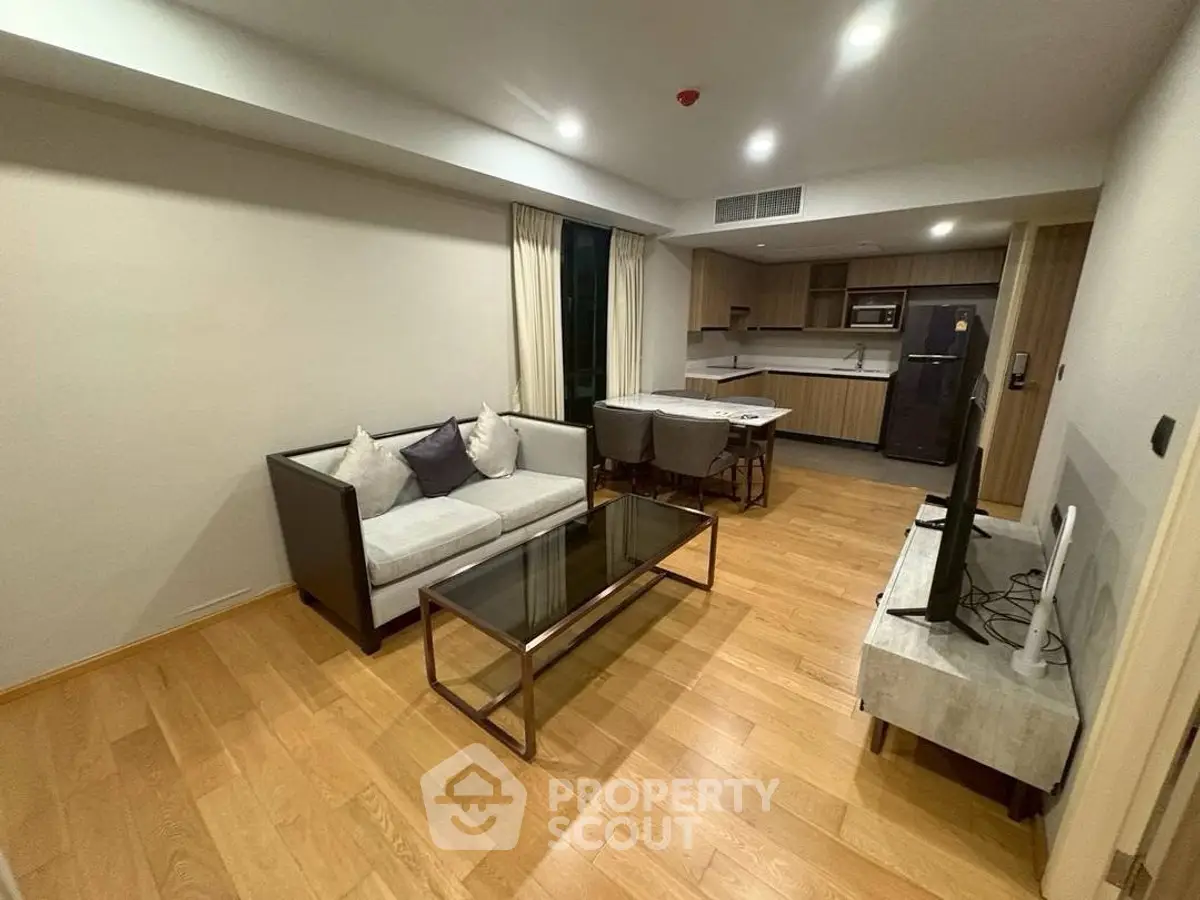 Modern living room with open kitchen, wooden flooring, and stylish furniture in a cozy apartment.