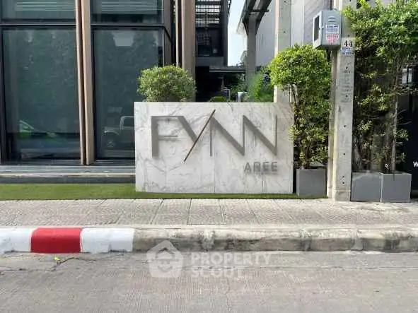 Modern building entrance with stylish signage and lush greenery, showcasing contemporary urban living.