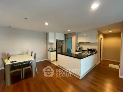 Modern kitchen with open layout and dining area featuring sleek cabinetry and hardwood floors.
