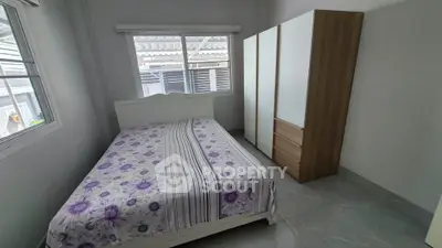 Cozy bedroom with floral bedding and large wardrobe, featuring ample natural light from a window.