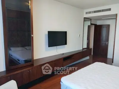 Spacious bedroom with modern wooden furniture and wall-mounted TV, perfect for relaxation.