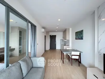 Modern open-plan living room with kitchen and dining area, featuring sleek furniture and natural light.