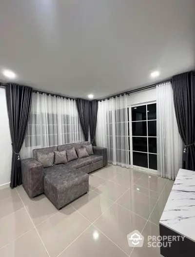 Modern living room with sleek gray sofa and elegant curtains in a bright, spacious setting.