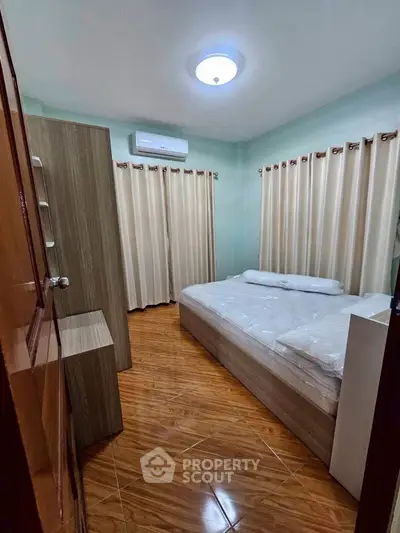 Cozy bedroom with wooden flooring, air conditioning, and ample natural light from large windows.