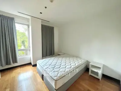 Bright bedroom with large window and hardwood floors, featuring a comfortable bed and modern decor.