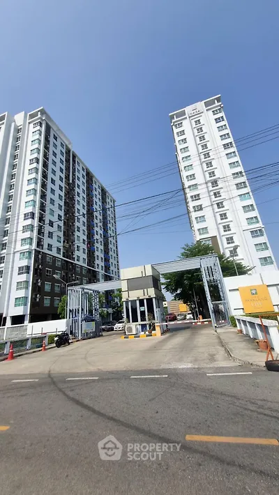 Modern high-rise condominium entrance with security gate and tall buildings under clear blue sky.