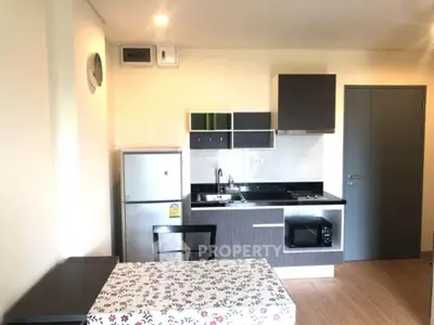 Modern kitchen with sleek cabinets, compact fridge, and dining area in a cozy apartment setting.