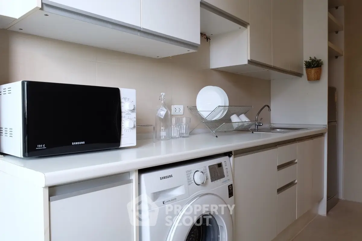 Modern kitchen with washing machine and microwave, sleek white cabinetry.