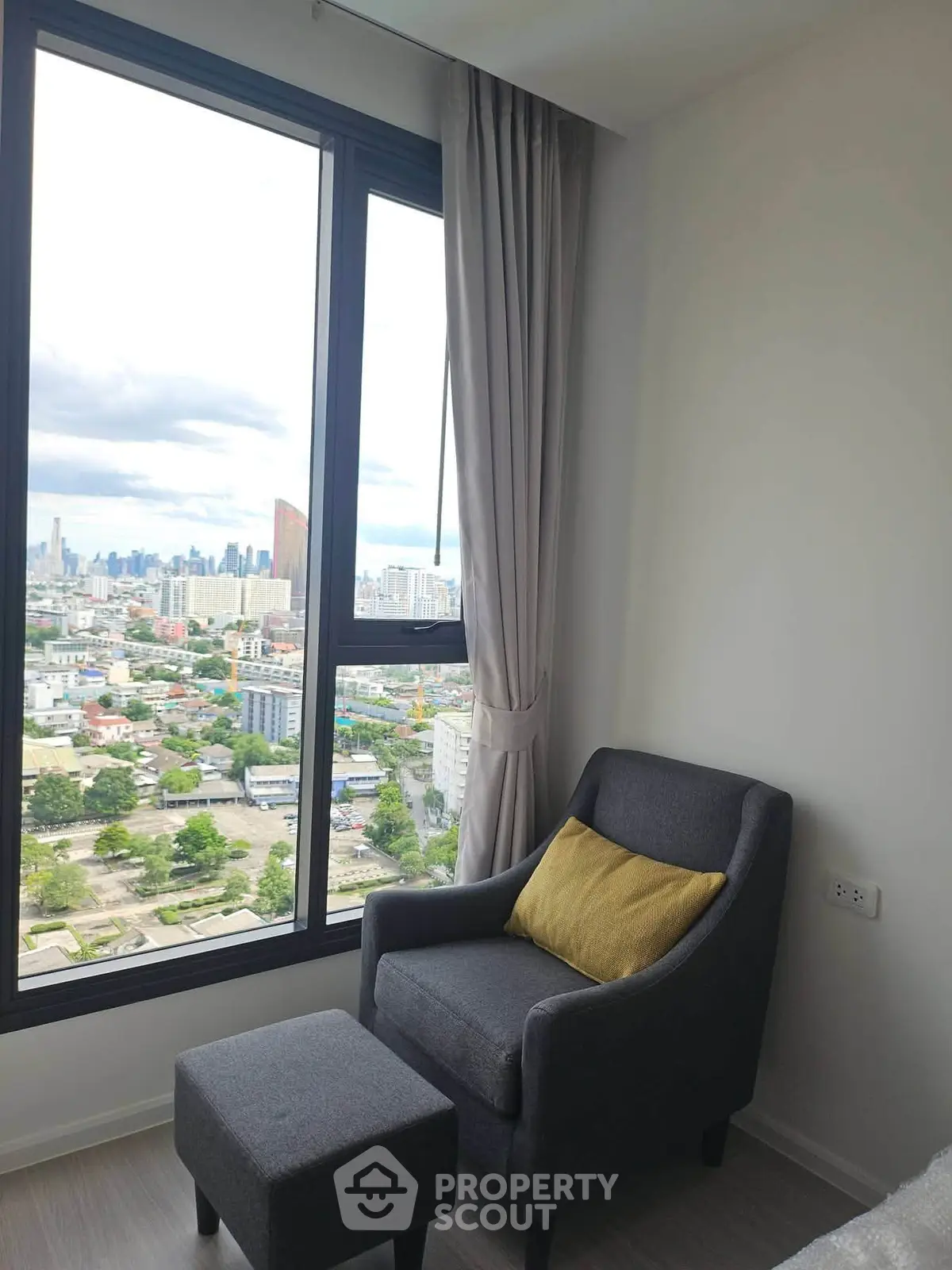 Cozy corner with armchair and city view from high-rise apartment window.