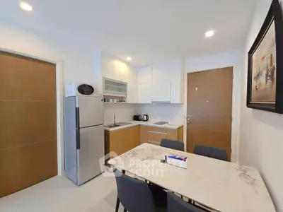 Modern kitchen with sleek design, featuring a dining table, refrigerator, and ample storage space.
