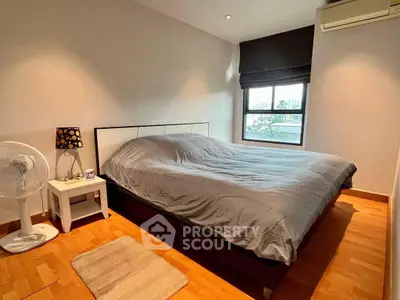 Cozy bedroom with wooden flooring and modern decor in a well-lit apartment.