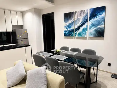 Modern dining area with sleek glass table and stylish kitchen in open layout apartment.