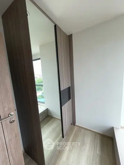 Modern bedroom with sleek mirrored wardrobe and large window offering natural light and city view.