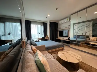 Modern studio apartment with stylish decor, featuring a cozy bed, sofa, and workspace with large windows.